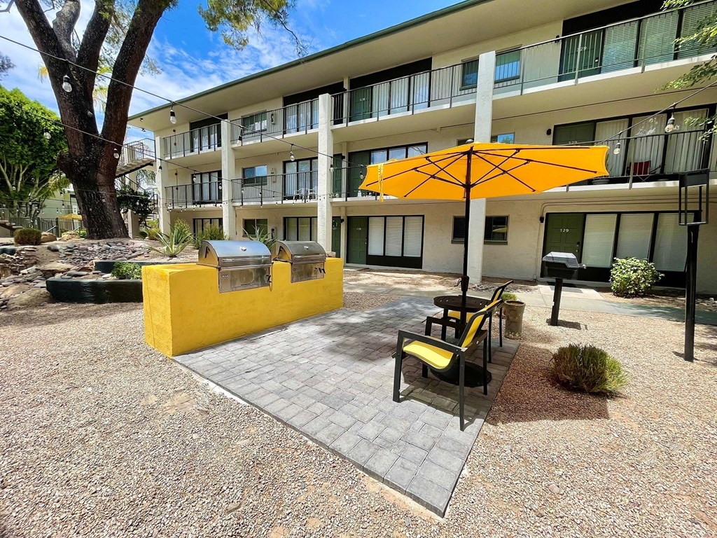 a patio with a yellow table and chairs and a barbecue grill