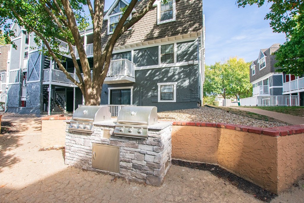 an outdoor kitchen with a grill and a tree in front of an apartment building