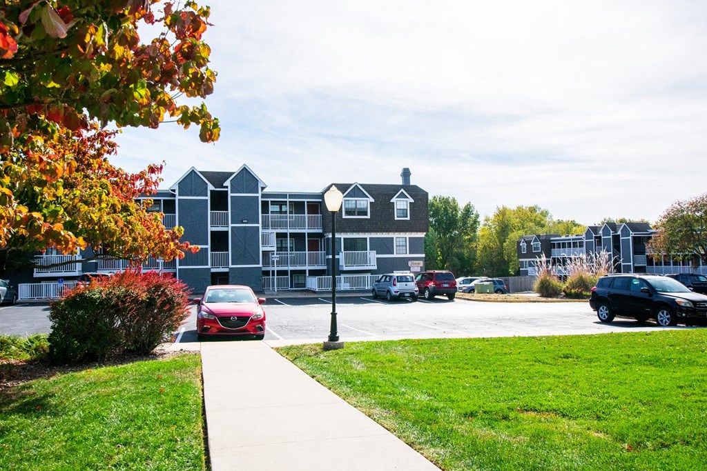 a sidewalk leading to a parking lot with a building in the background