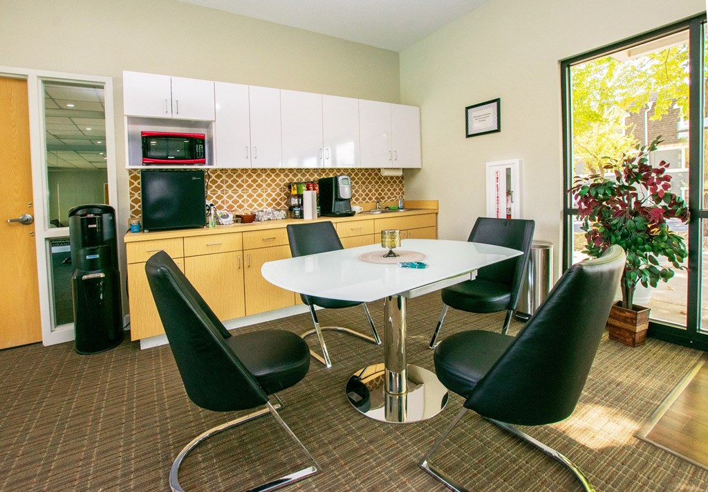 a room with a table and chairs and a kitchen in the background
