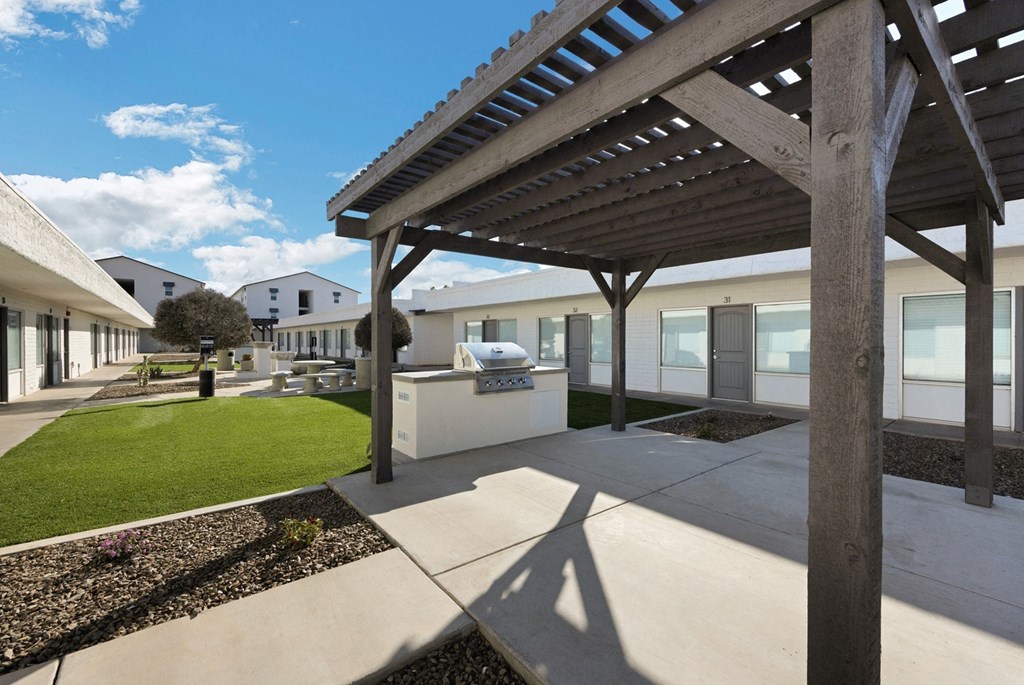 a covered patio with a grill and a lawn in front of a building