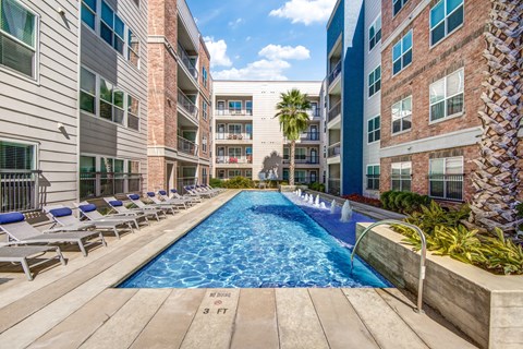a swimming pool with chaise lounge chairs and palm trees in front of an apartment building at Republic at Alamo Heights, Texas