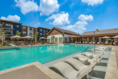 A large swimming pool with sun loungers and a building in the background.