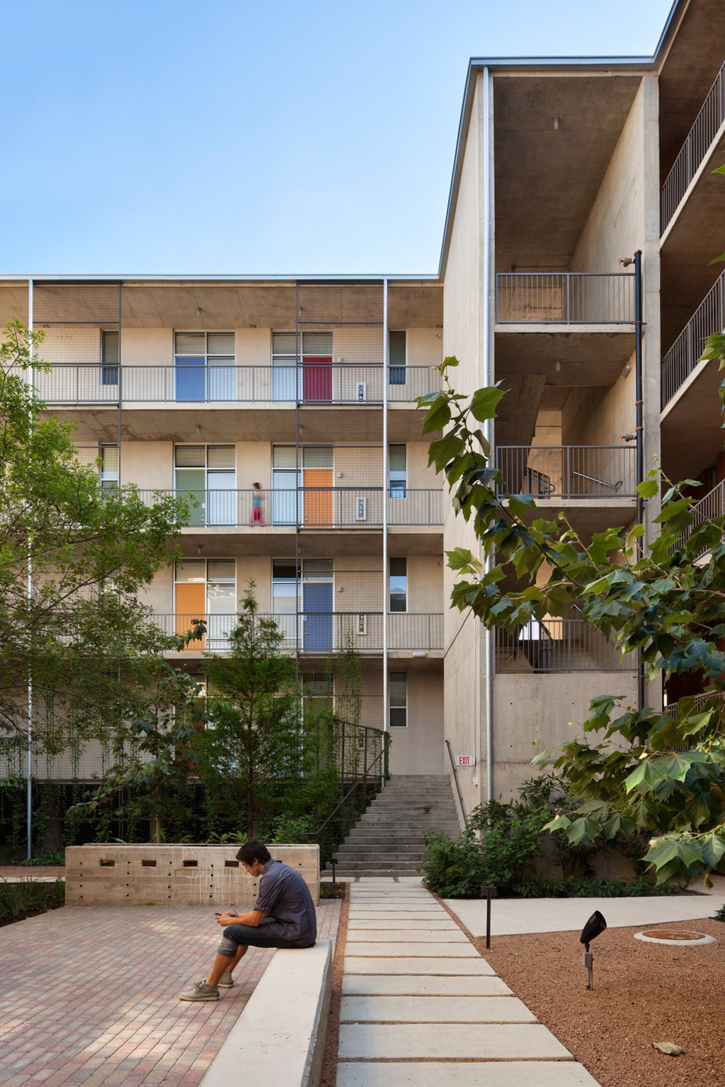 A man sits on a bench in front of a building with balconies.