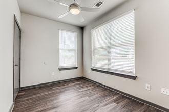 an empty bedroom with two windows and a ceiling fan