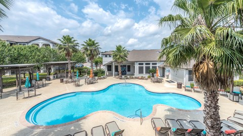 A large outdoor swimming pool surrounded by lounge chairs and palm trees at Rosemary Apartments, Conroe, TX, 77384