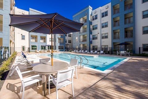 A pool area with a table and chairs and a pool umbrella.