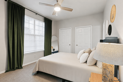 A bedroom with a bed, a ceiling fan, and a window with green curtains.