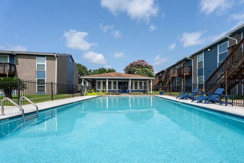 A swimming pool in front of a building with a patio and chairs.