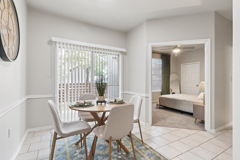 A dining room with a table set for two and a bedroom in the background.