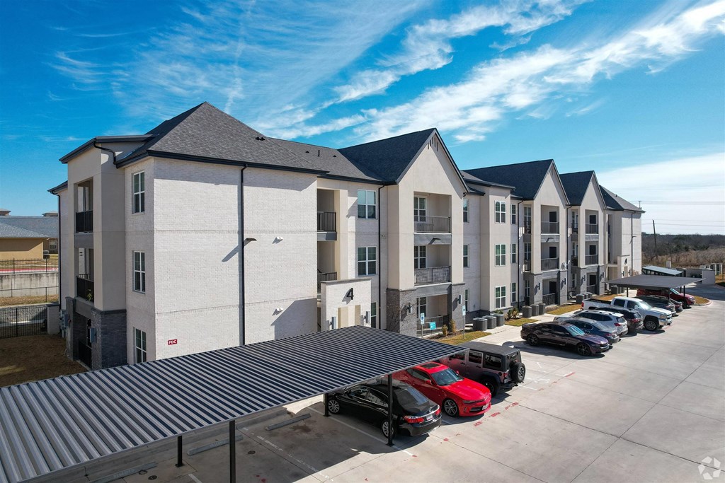 a row of apartment buildings with cars parked in front of them a row of apartment buildings with cars parked in front of them at The Fitzroy San Marcos, Texas
