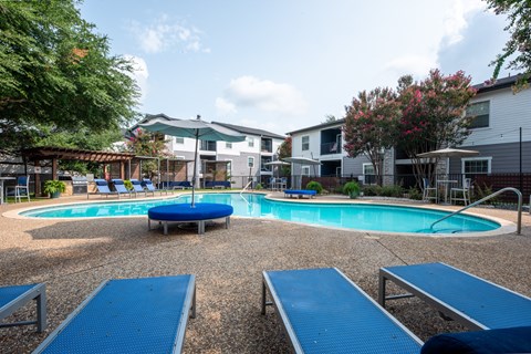 A round blue pool surrounded by a gravel area and a few chairs.