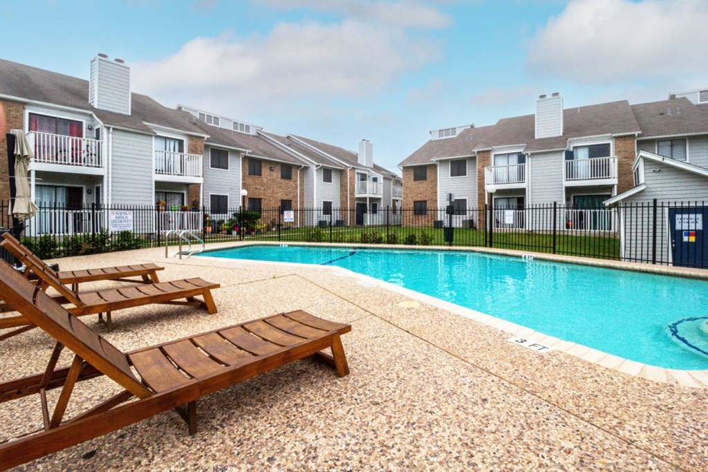 a swimming pool with two wooden benches next to an apartment building at Northchase, Austin, TX