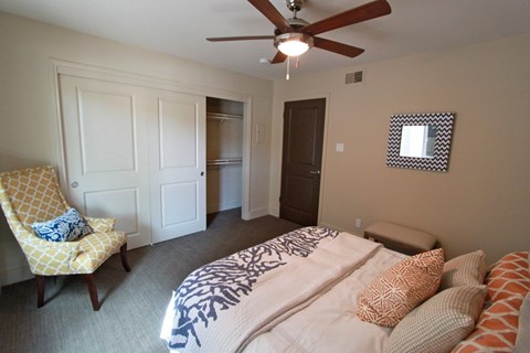 A bedroom with a bed, chair, and a ceiling fan.