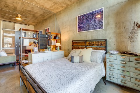 Industrial loft bedroom with exposed concrete walls at 1221 Broadway Lofts Apartments, Texas