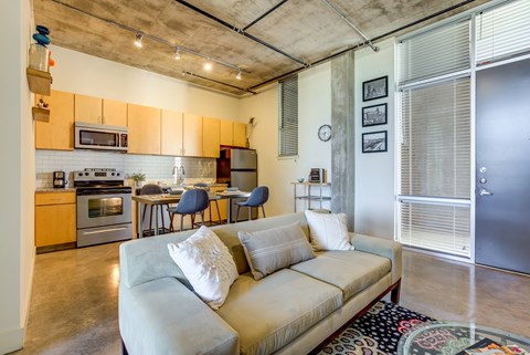 A living room with a couch and a kitchen area in the background.