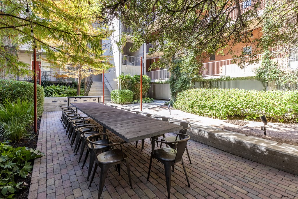 A long table with chairs is surrounded by green plants.