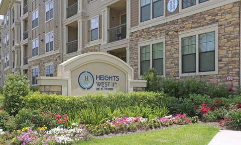 The front of the Heights West apartment complex is shown with a well-maintained garden in the foreground.