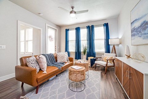 a living room with a brown couch and blue curtains at The Landings at Brooks City-Base, San Antonio, 78235
