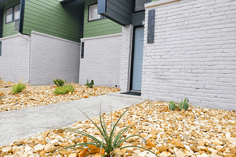a sidewalk in front of a building with gravel and plants