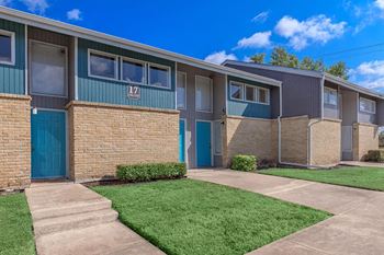 an apartment building with blue doors and a grass yard