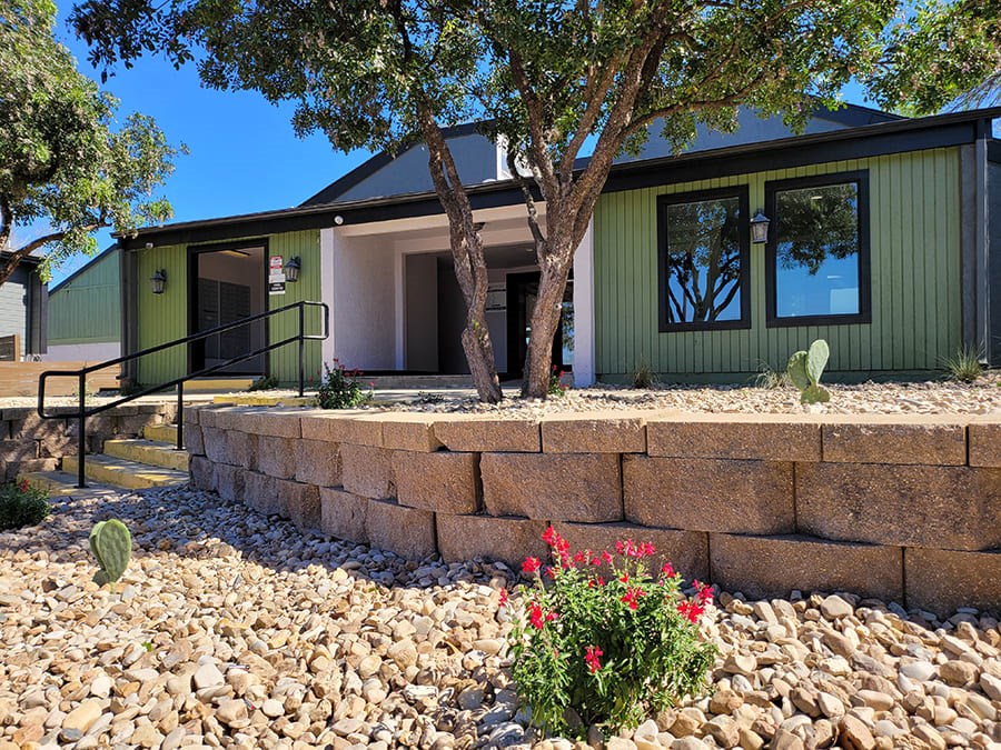 a house with a stone retaining wall and a tree in front of it