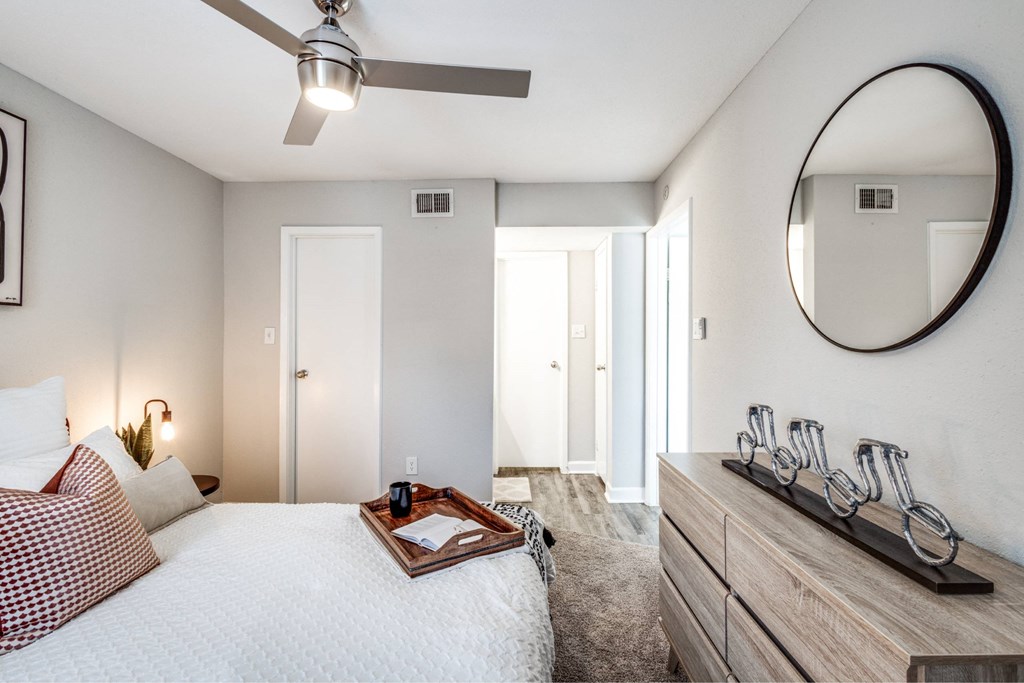 A bedroom with a bed, dresser, mirror, and ceiling fan.
