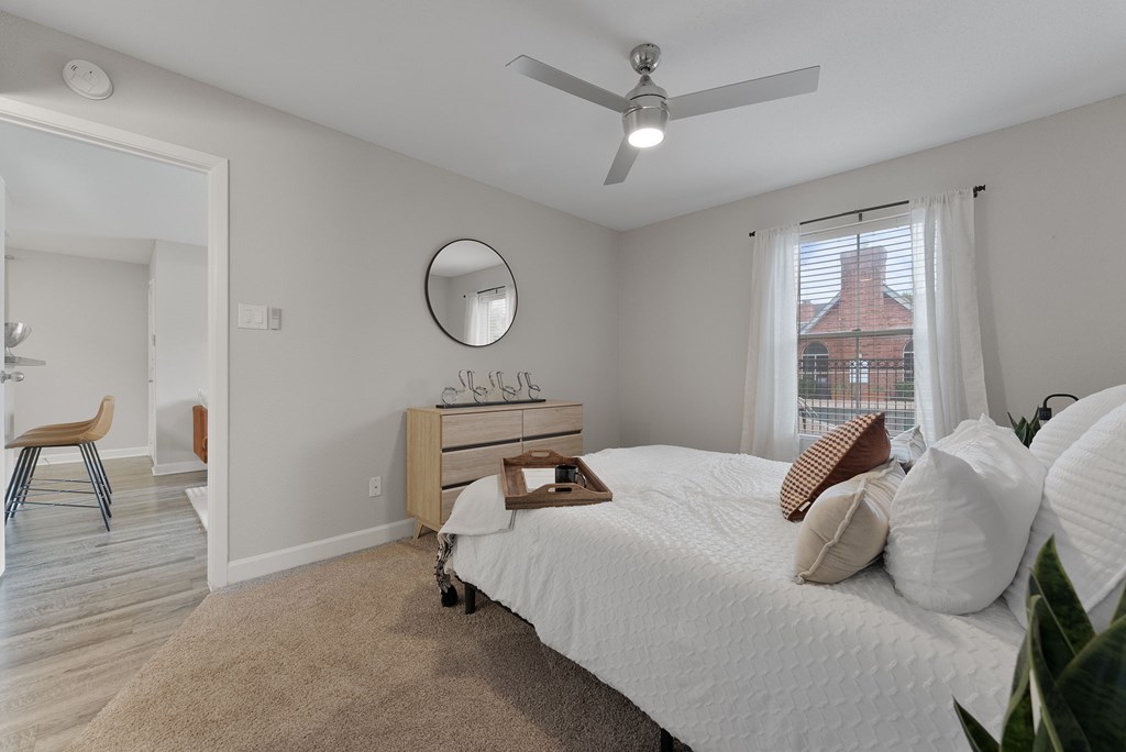 A bedroom with a white bed and a window with white curtains.