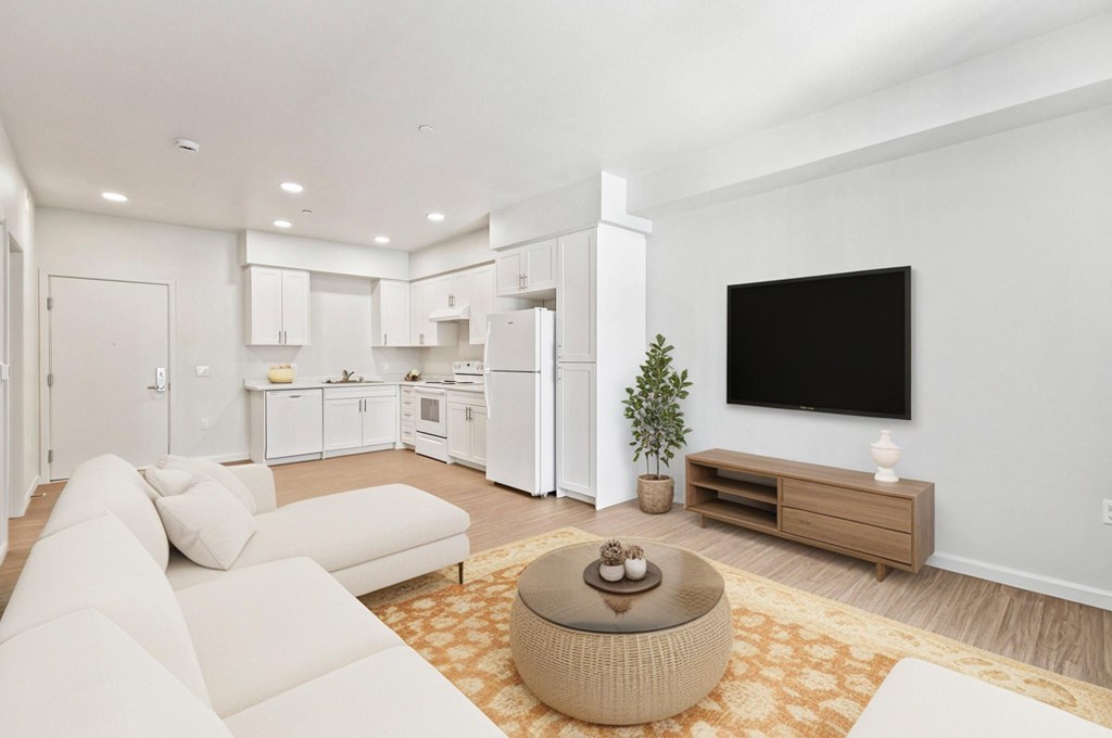 A modern living room with a white couch, a brown ottoman, and a flat-screen TV mounted on the wall.