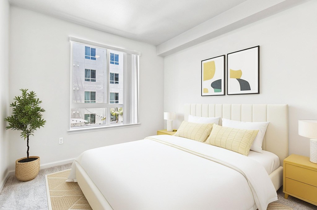 A bedroom with a large bed, a potted plant, and two framed pictures on the wall.