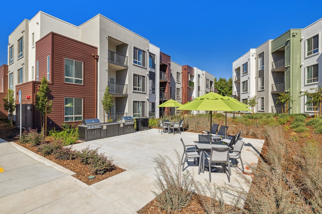 an outdoor patio with tables and umbrellas in front of an apartment building