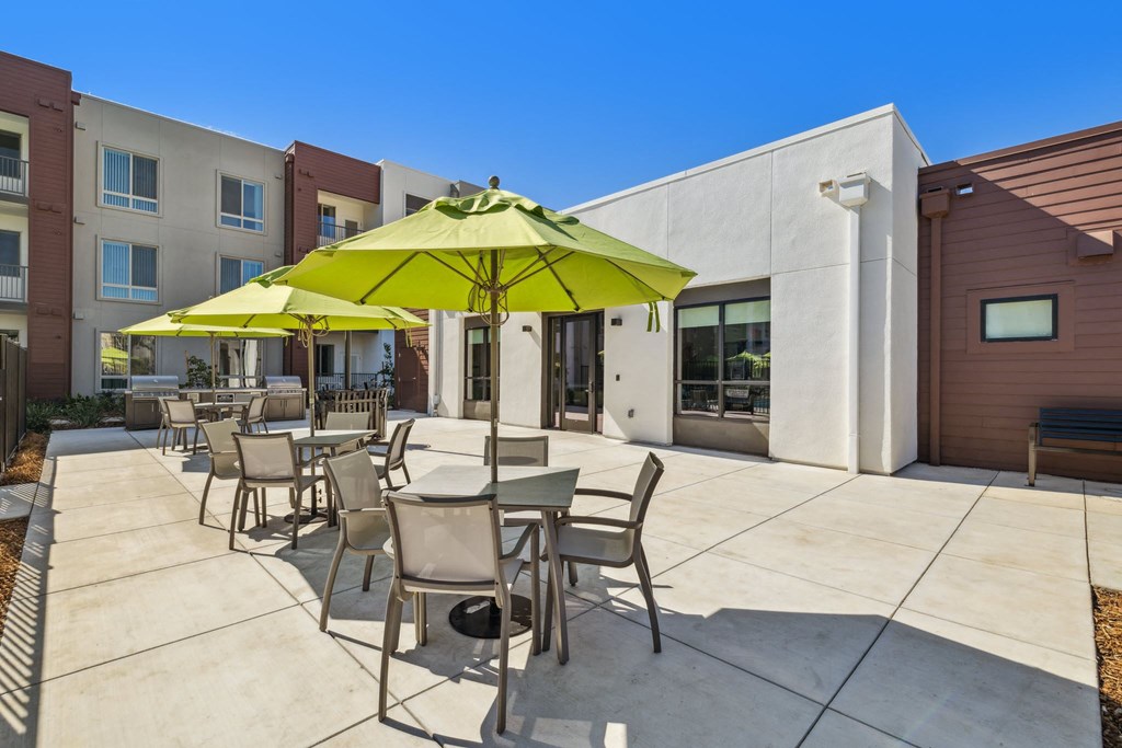 our patio has tables and chairs with umbrellas and a building in the background
