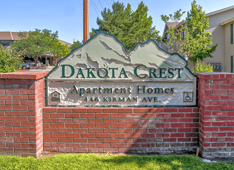A sign for Dakota Crest Apartment Homes stands in front of a brick wall.