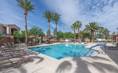 A pool surrounded by palm trees and lounge chairs.