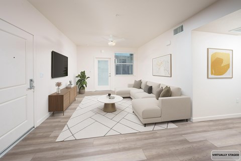 A living room with a white couch, a coffee table, and a TV on the wall.