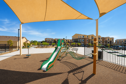 A playground with a green and white slide under a yellow canopy.