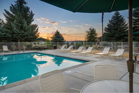 A pool surrounded by chairs and trees with a sunset in the background.