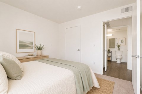 A bedroom with a bed, a nightstand with a plant, and a painting on the wall.