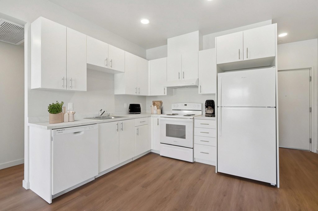 A white kitchen with wooden floors and white appliances.at Mainline North | Affordable Apartments, Santa Clara, CA