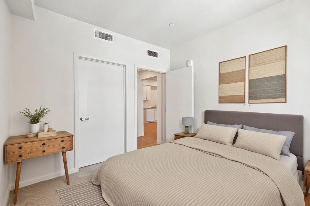 A bedroom with a bed, nightstand, and a plant on a wooden table.