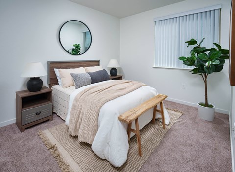 a bedroom with a white bedspread and a round mirror on the wall