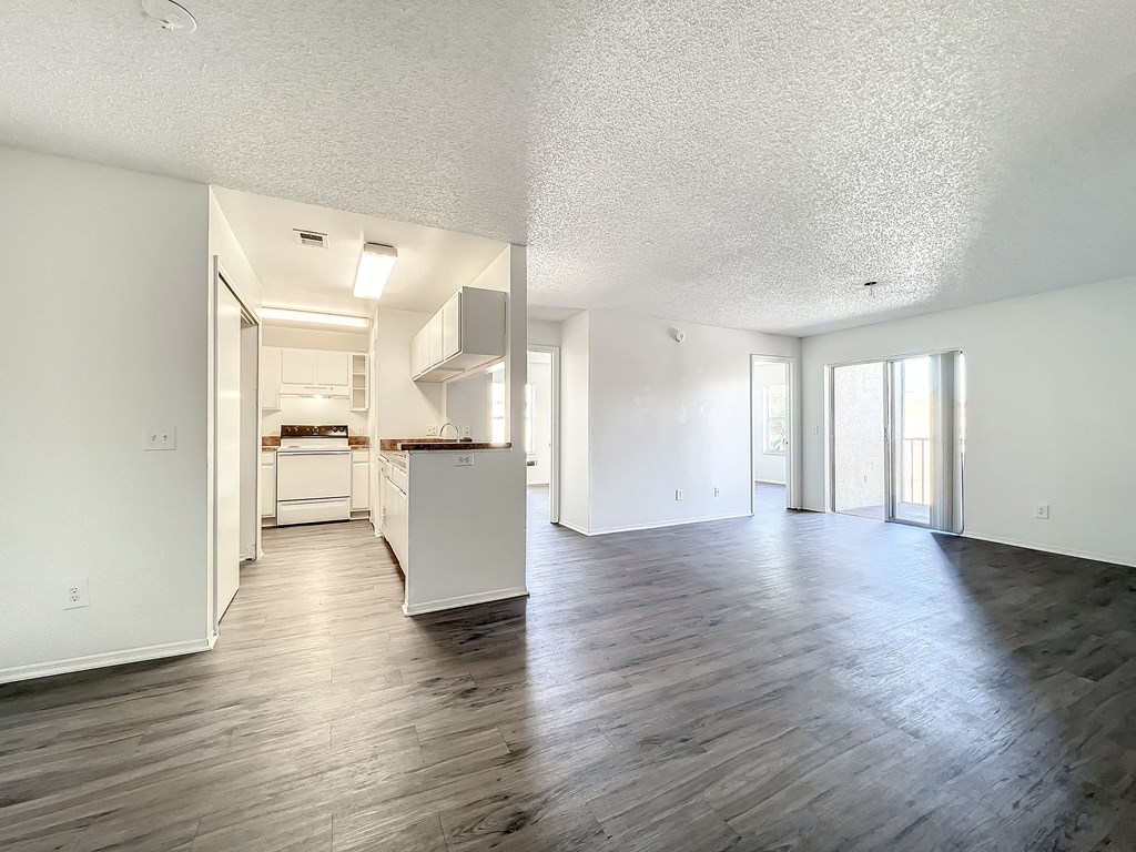 an empty living room with a kitchen in the background