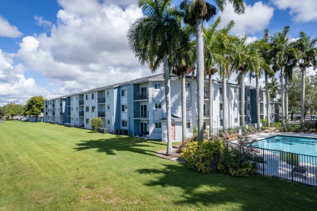 an apartment building with a pool in the foreground and palm trees in the background