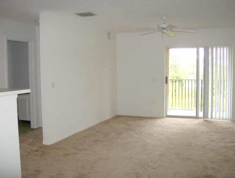 an empty living room with a ceiling fan and a balcony