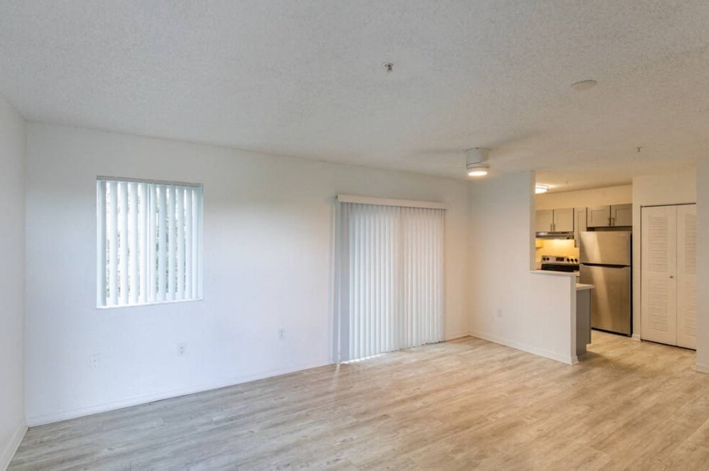 an empty living room with a kitchen in the background