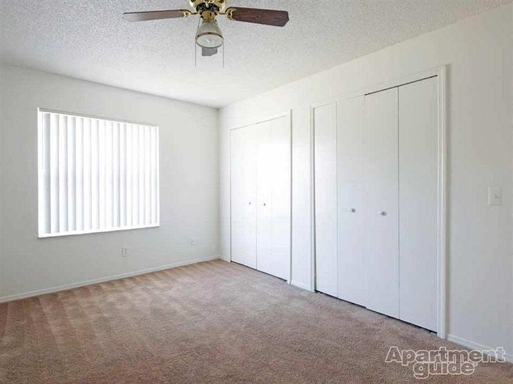 an empty living room with a ceiling fan and white closets