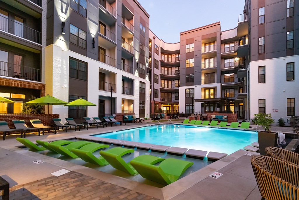 a swimming pool with green lounge chairs and umbrellas in front of an apartment buildingat Abberly Foundry Apartment Homes, Nashville