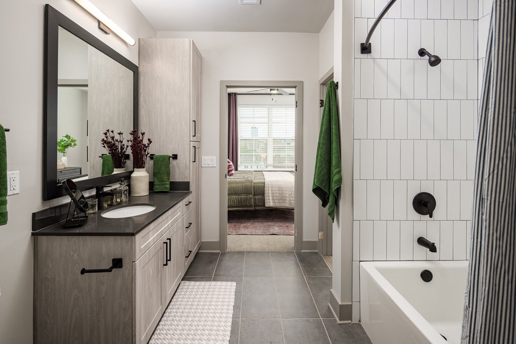 a bathroom with white tile walls and a black countertop with a sink and a bathtub at Abberly Foundry Apartment Homes, Nashville, 37203