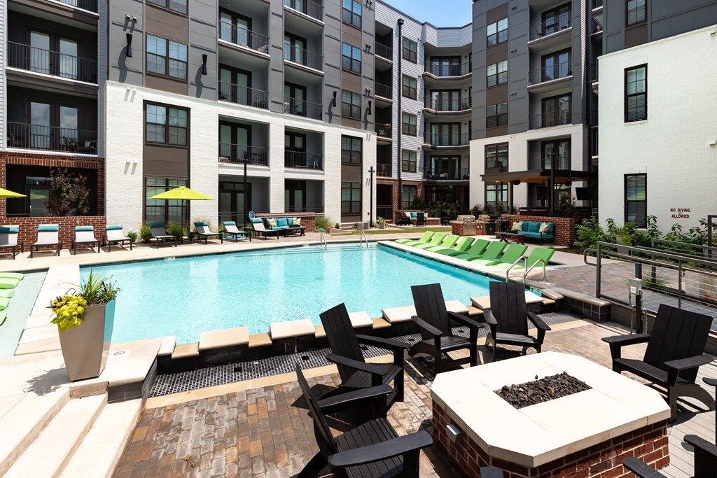 an outdoor swimming pool with lounge chairs and a fire pit in front of an apartment building at Abberly Foundry Apartment Homes, Nashville, 37203