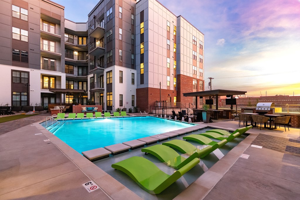 a swimming pool with green lounge chairs in front of an apartment building at Abberly Foundry Apartment Homes, Nashville, TN
